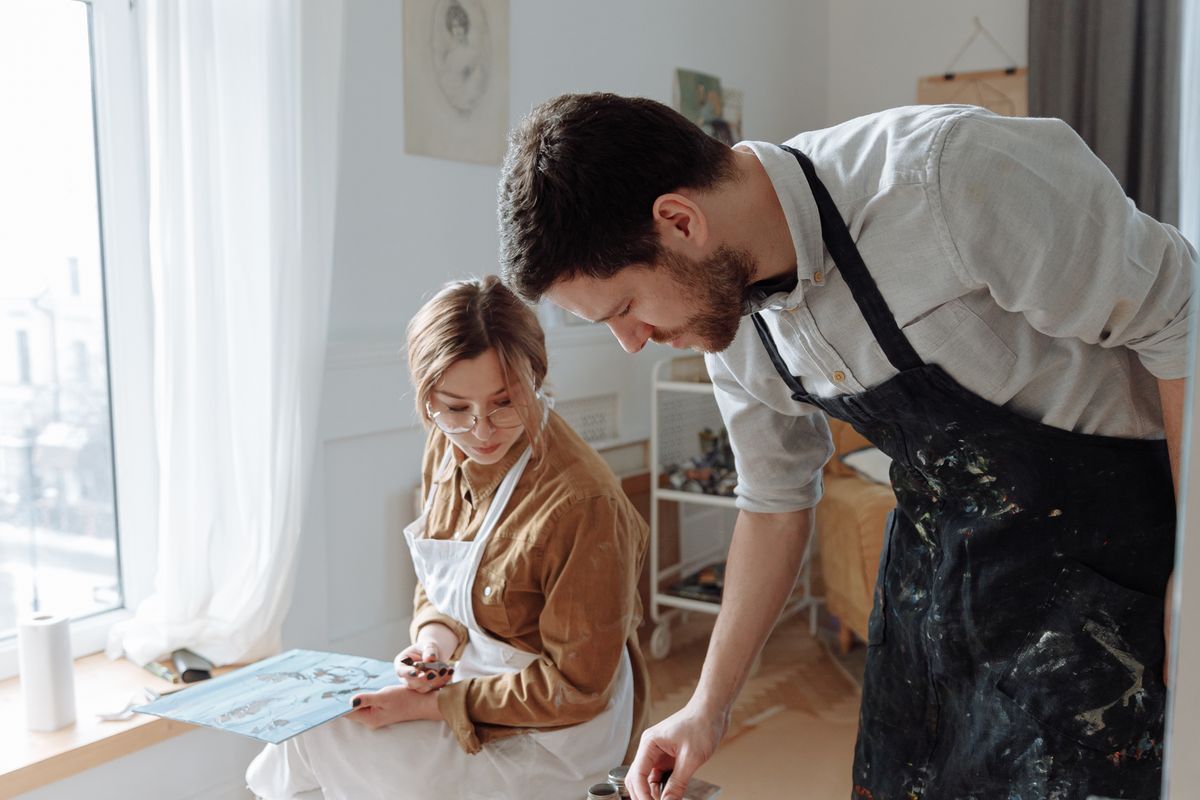 Two colleagues absorbed in painting together beside a bright studio window