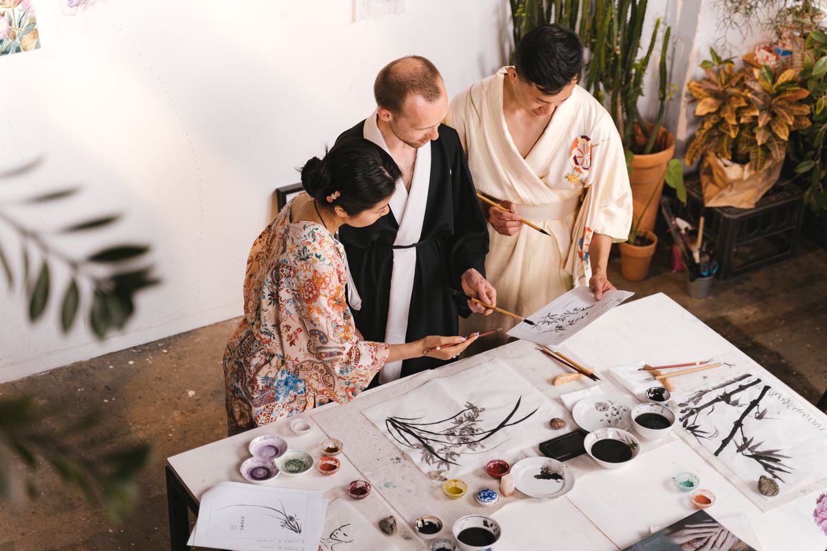 Three colleagues focused on an ink painting laid across a shared table